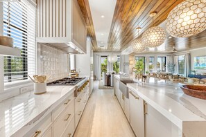 A modern kitchen with a long island, wooden ceiling, and pendant lights.
