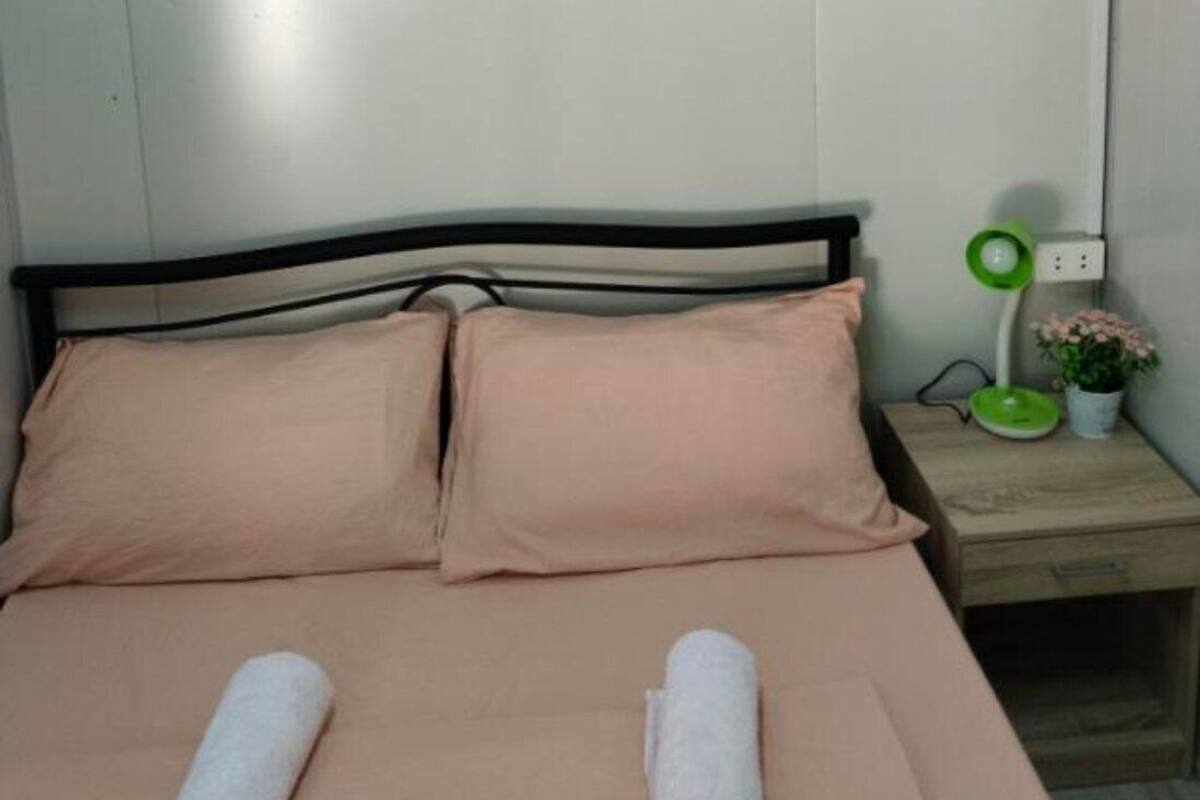 A bed with two pillows, a green lamp, and a small plant on a bedside table.