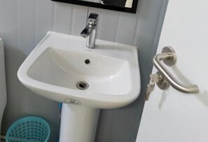 A white pedestal sink with a single faucet, a wall-mounted mirror above it, and a door handle to the right.