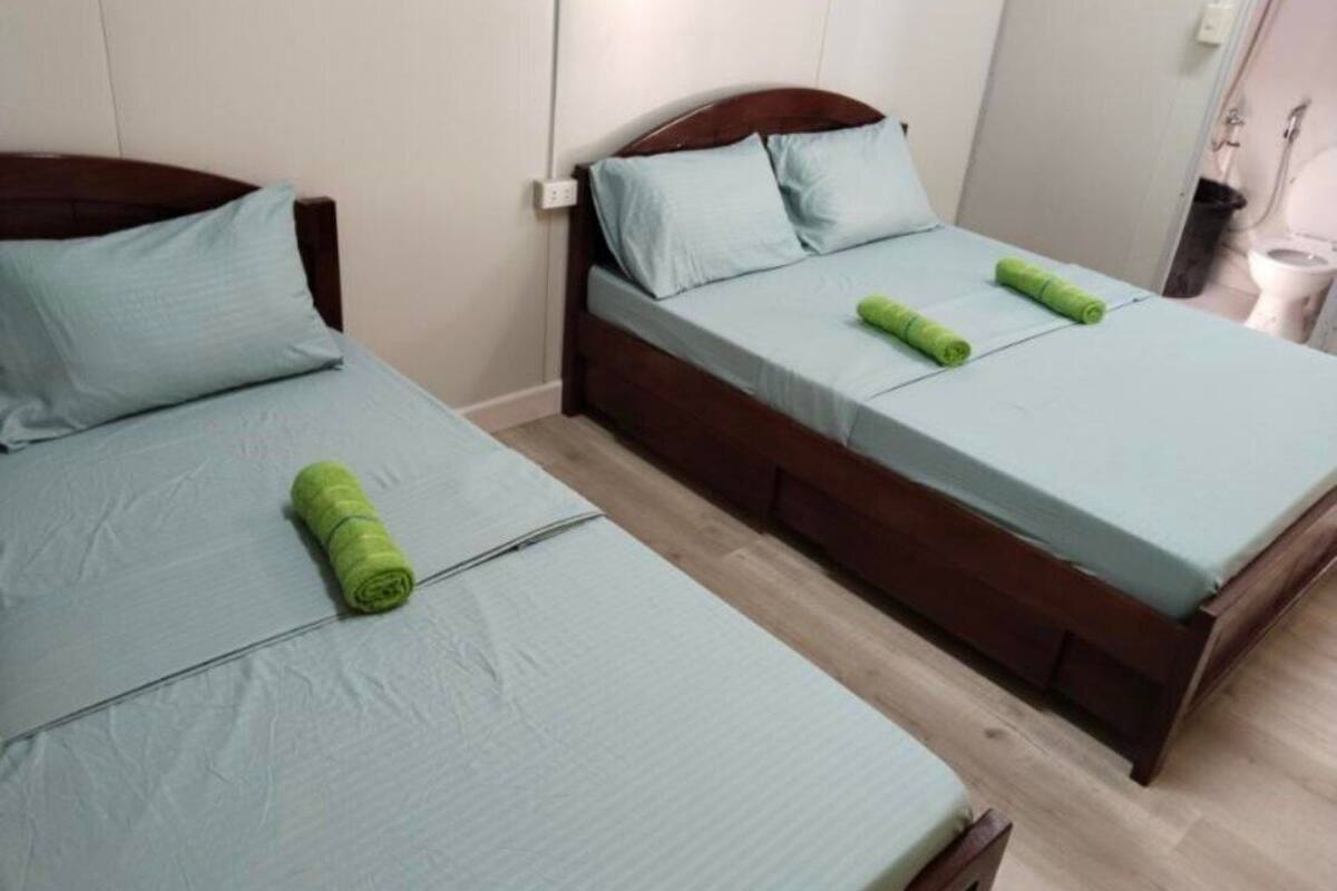 Two single beds with wooden frames and light blue bedding, a wooden floor, and a white wall with a light switch.