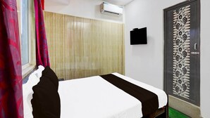 Una camera da letto con un letto, una finestra con tende, un condizionatore d'aria, una TV a parete e una porta decorativa.