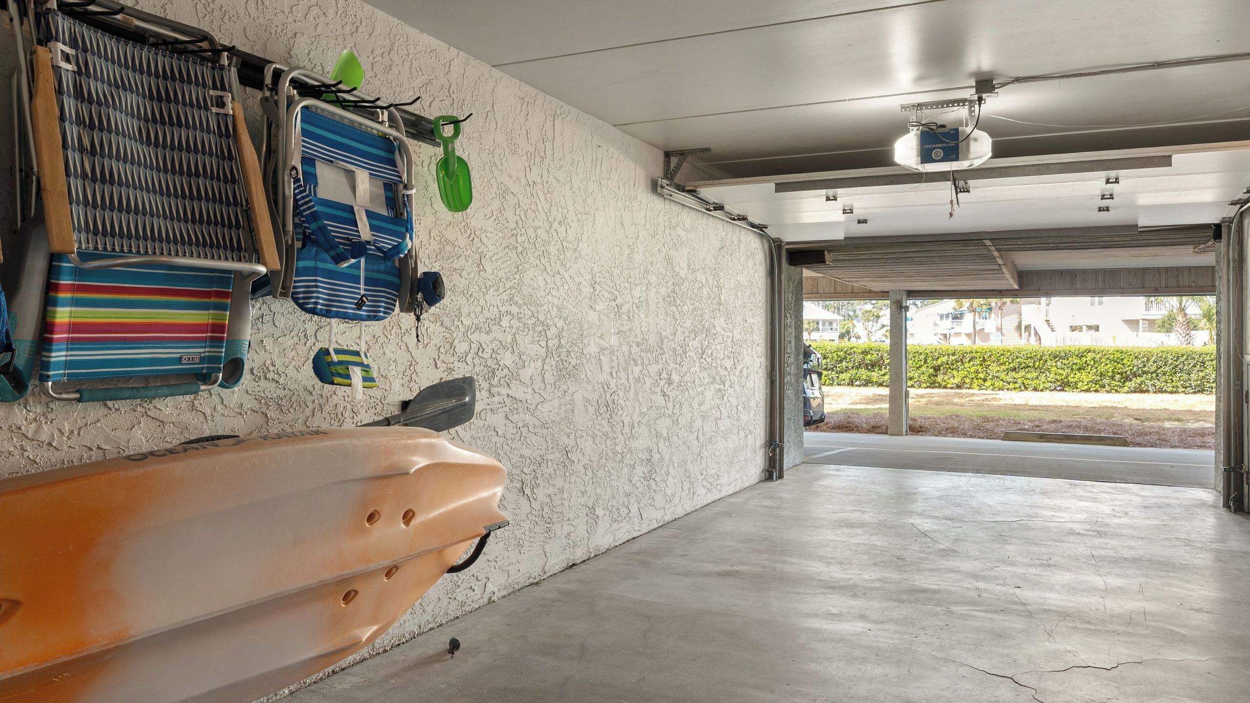 A garage with a concrete floor, a kayak, and various bags and paddles hanging on the wall.