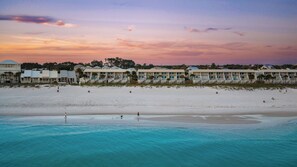 Ein Strandhotel mit mehrstöckigen Gebäuden, einem sandigen Strand und klarem, türkisblauem Wasser.