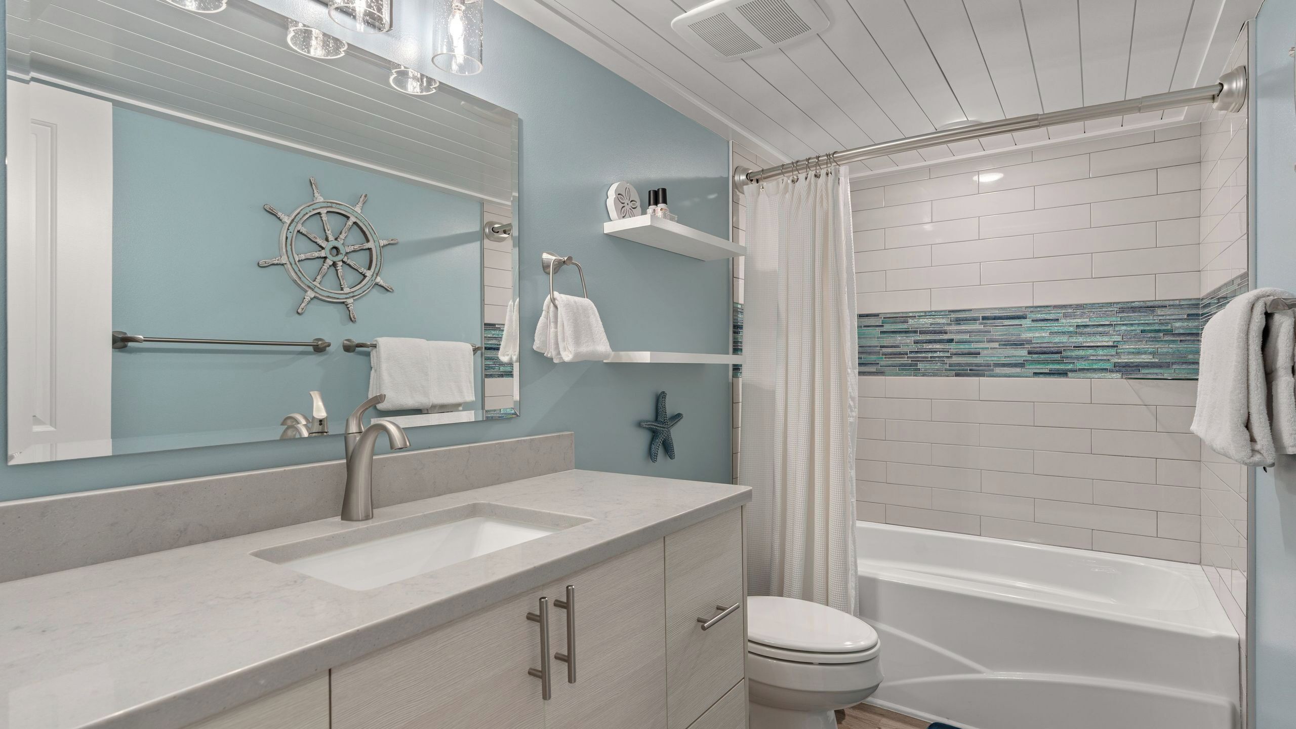 A bathroom with a vanity, sink, mirror, and a shower area.