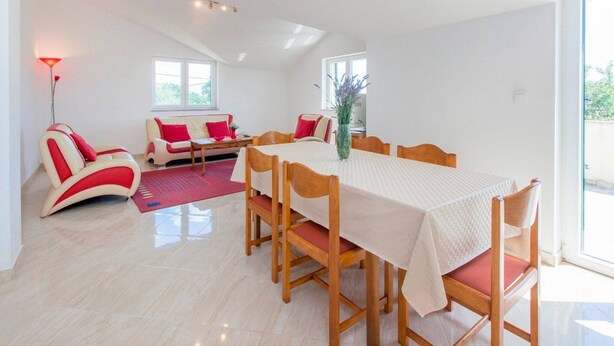 Een eethoek met een tafel voor vier personen, houten stoelen, een rode bank en een rode lamp.