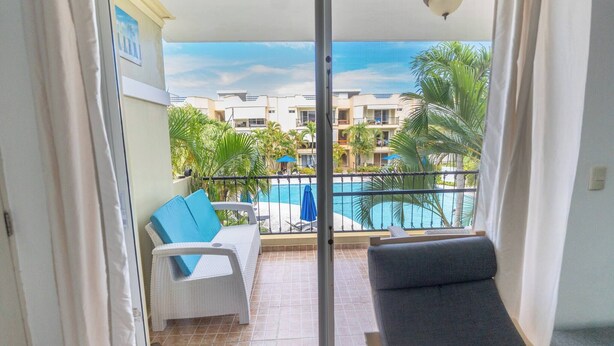 Ein Balkon mit Blick auf einen Swimmingpool, weißen Korbmöbeln und einem grauen Sofa.