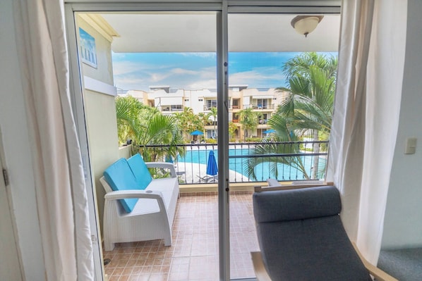 A balcony with a view of a swimming pool, white wicker furniture, and a grey sofa. - Garden Condos APT 3 Affordable 1BR APT in Sosua (Sosúa)