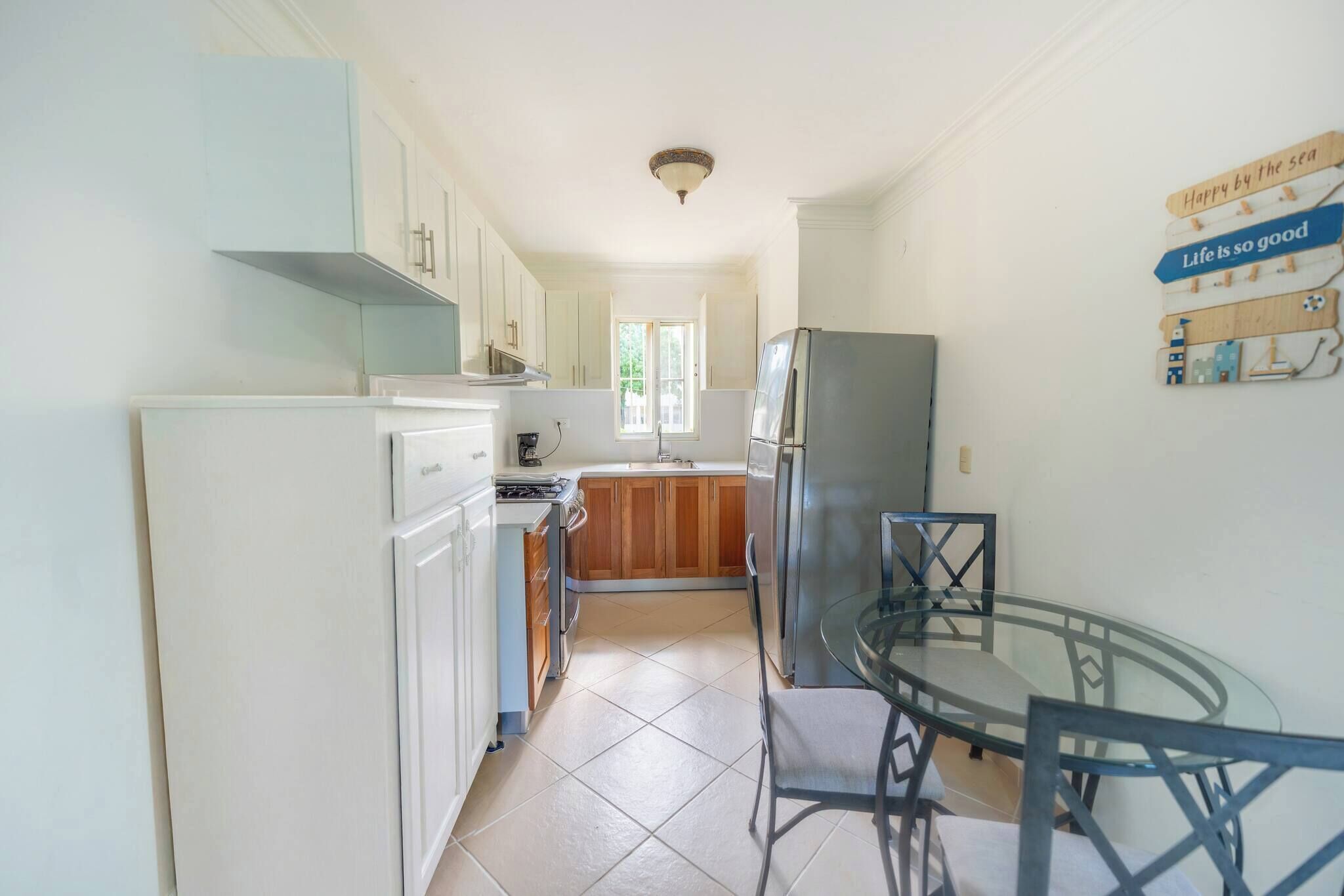 A kitchen with white cabinets, a stainless steel refrigerator, a glass dining table, and a window.