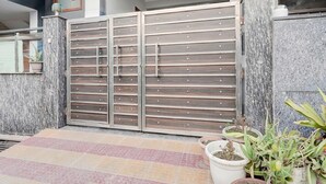 A gated entrance with a metal gate, potted plants, and a tiled pathway. - Super Collection O Sector 20 Noida (Noida)