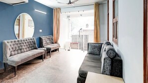 A room with a large mirror, two sofas, a ceiling fan, and a view of the outside. - Super Collection O Sector 20 Noida (Noida)
