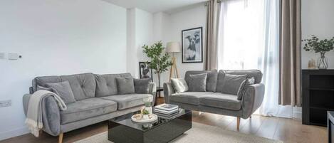 A modern living room with two grey sofas, a coffee table, and a bookshelf.