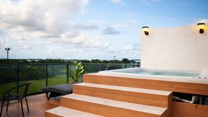 Un bain à remous sur une terrasse en bois, avec des marches menant à celui-ci, une chaise et une plante en pot.