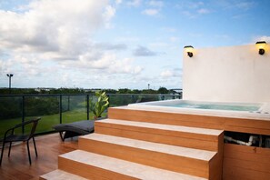 A hot tub on a wooden deck with steps leading up to it, a chair, and a potted plant. - 2BR with JacuzziRooftop & Golf View (Punta Cana)