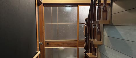 A narrow hallway with wooden flooring, a glass door, and a wooden staircase with shelves.