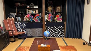 Um espaço com tatames, uma mesa de madeira, almofadas, um globo e uma estante com objetos decorativos.