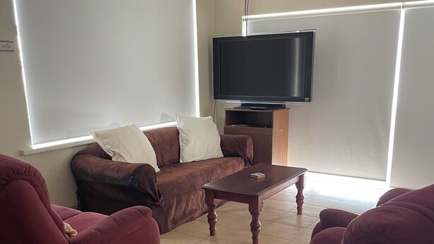 Ein Wohnzimmer mit einem braunen Sofa, zwei roten Sessel, einem Holztisch und einem flachbildfernseher an der Wand.