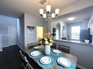 Un coin repas avec une table en bois dressée pour six personnes, un lustre et un vase rempli de fleurs.