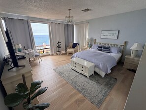 Ein Schlafzimmer mit Bett, Nachttischen, einem Schreibtisch, einem Sessel und Meerblick.