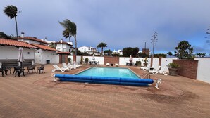 A swimming pool with lounge chairs and tables, surrounded by a brick patio and white buildings with red-tiled roofs. - VILLA ESPERANZA — OCEANFRONT LIVING WHERE THE FAIRWAY MEETS THE SEA (Ensenada)
