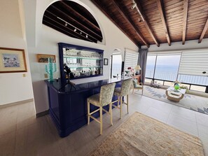Eine Bar mit Theke, Stühlen und Meerblick.