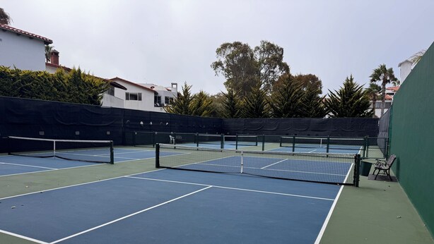 A tennis court with multiple courts, a net, and a green wall. - VILLA ESPERANZA — OCEANFRONT LIVING WHERE THE FAIRWAY MEETS THE SEA (Ensenada)