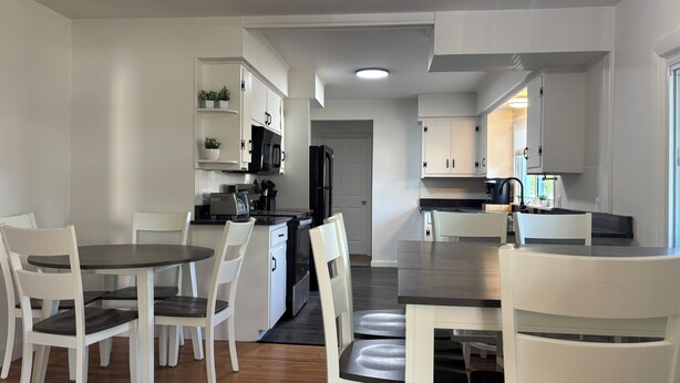 A modern kitchen with white cabinetry, a dining area with white chairs, and a black countertop. - Gillette Getaway in Milford - Sleeps 16 (Milford)