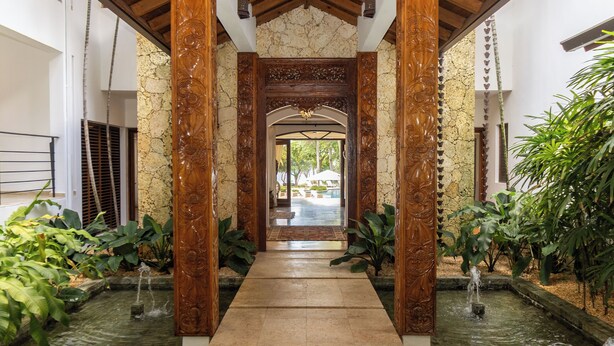 A corridor with ornate wooden pillars, a stone wall, and a water feature. - Casa Delmar: Private Beachfront Estate with Chef, 2 Butlers ,Staff & Ocean Views (La Romana)
