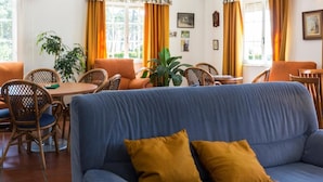 Una habitación con sofá azul, sillas anaranjadas, una mesa de comedor y una ventana con cortinas.