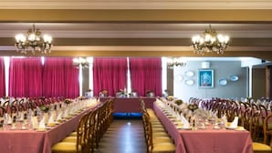 Un salón de banquetes con mesas largas, candelabros y vistas al exterior.