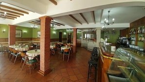 Un restaurante con varias mesas y sillas, una zona de bar y una cocina al fondo.