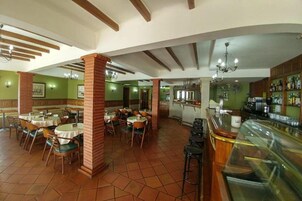 Un restaurante con varias mesas y sillas, una zona de bar y una cocina al fondo.