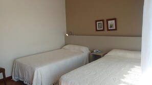 Une chambre d’hôtel avec deux lits simples, une table de chevet avec une lampe et un téléphone.