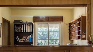 Un mostrador de recepción con detalles de madera, una estantería con archivadores, una ventana con vista a zonas verdes y un zapatero.