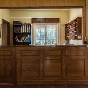 Un comptoir d’accueil avec un revêtement en bois, une bibliothèque avec des classeurs, une fenêtre donnant sur un espace verdoyant et un porte-chaussures.