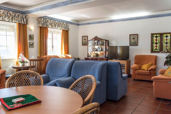 Un salon comprenant un canapé, des fauteuils, une table, un téléviseur et un miroir décoratif.