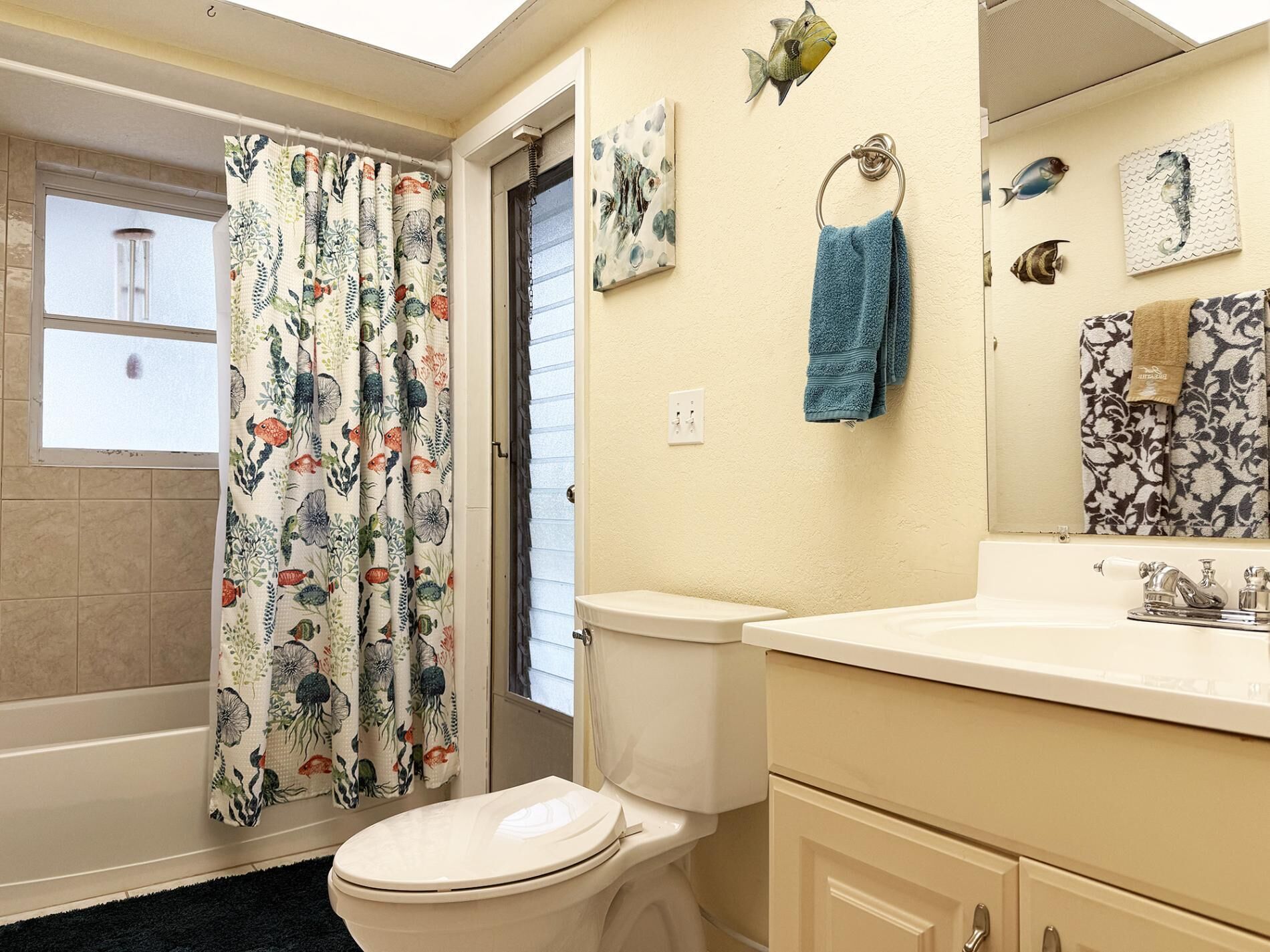 Ein Badezimmer mit Toilette, Waschbecken, Spiegel und einer Duschvorhang mit Blumenmuster.