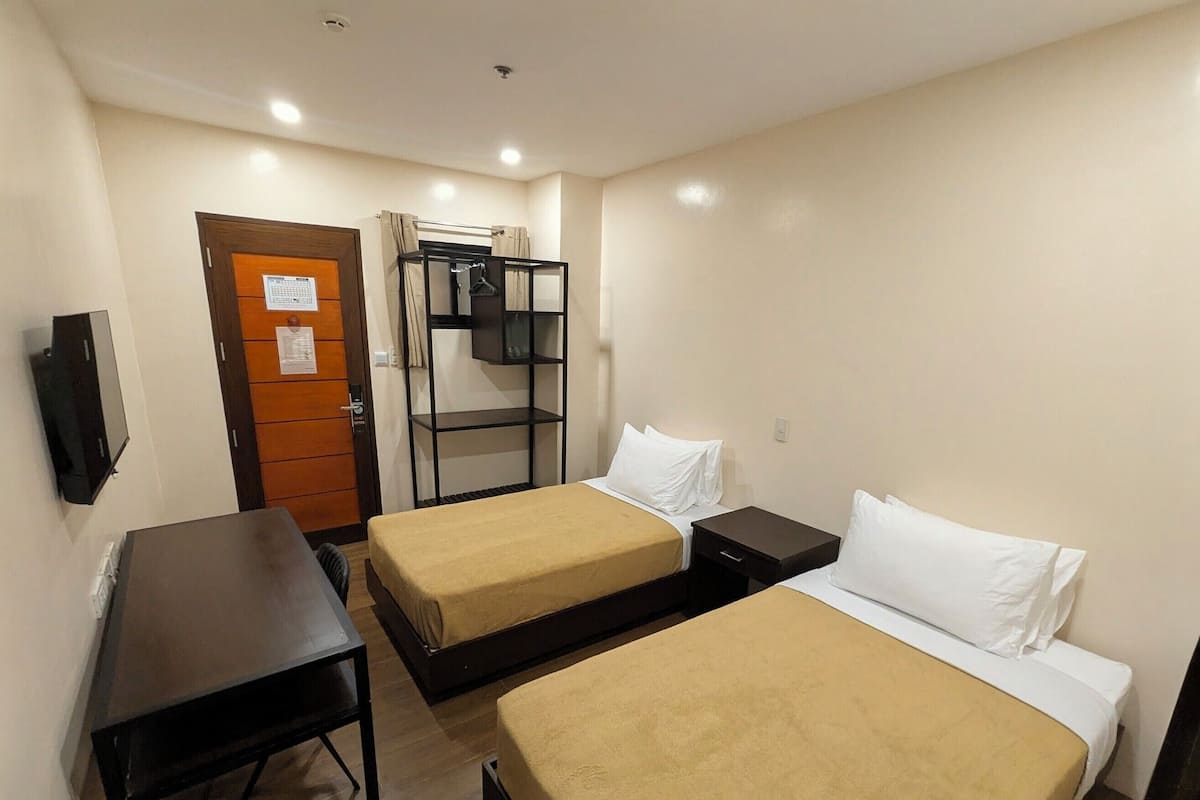 A hotel room with two beds, a desk, a wardrobe, and a TV.
