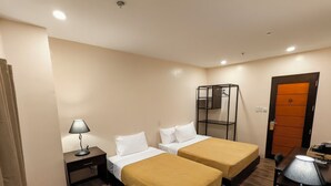 A hotel room with two beds, a desk, a chair, a lamp, a wardrobe, and a door.