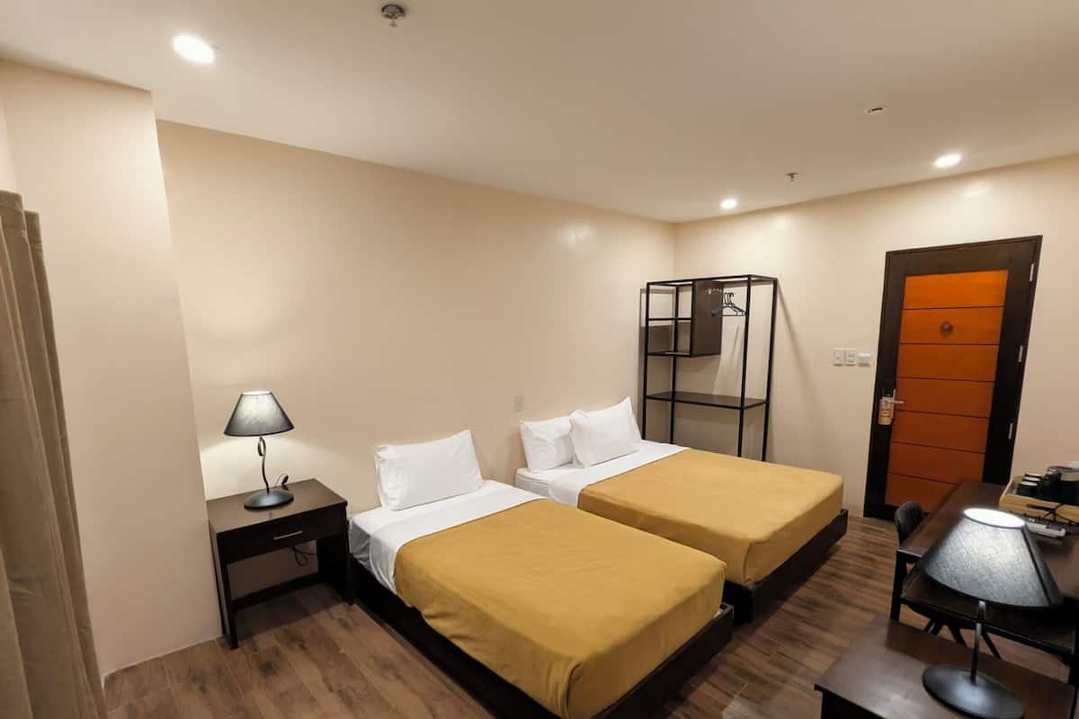 A hotel room with two beds, a desk, a chair, a lamp, a wardrobe, and a door.