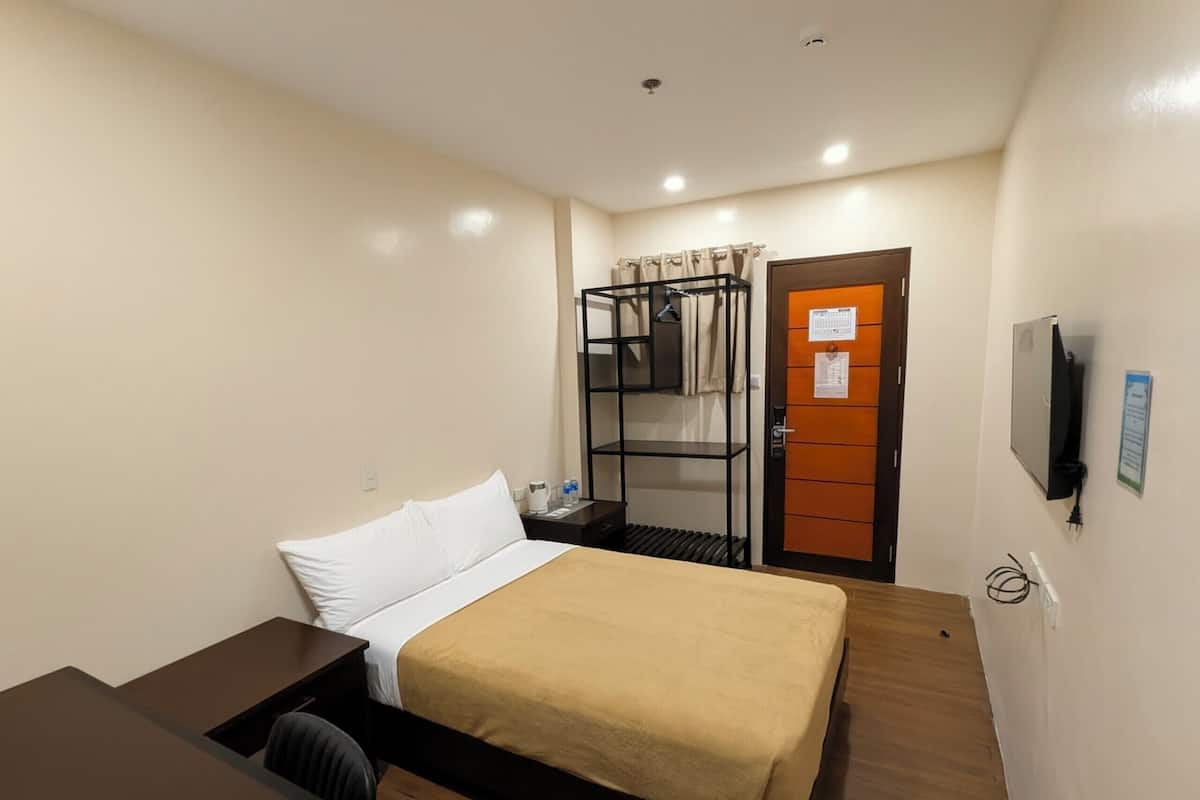 A hotel room with a bed, a desk, a wardrobe, a television, and a door with a calendar.