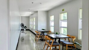 A spacious room with multiple tables and chairs, large windows, and a ceiling fan.