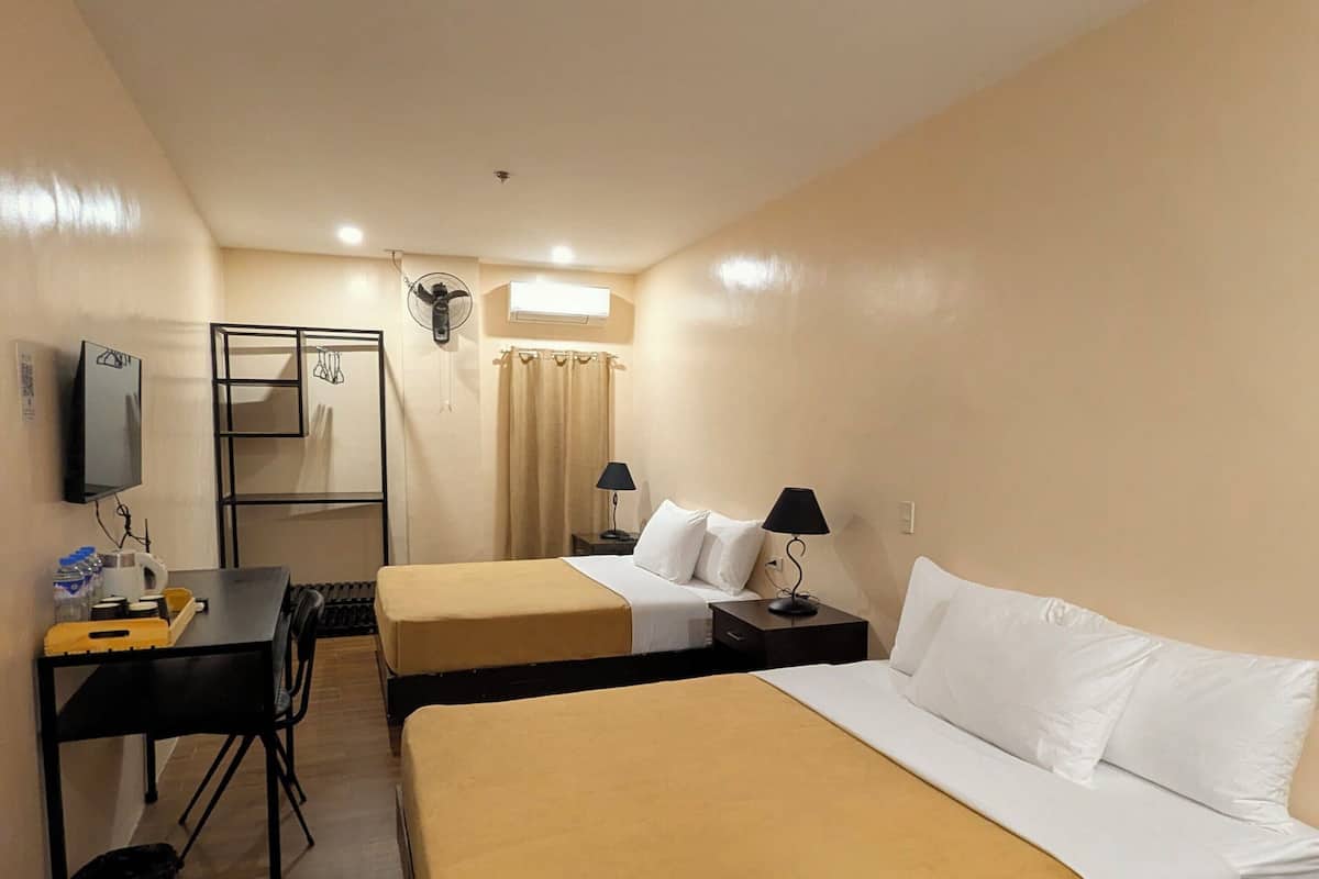 A hotel room with two beds, a desk with a chair, a TV, and a window with curtains.
