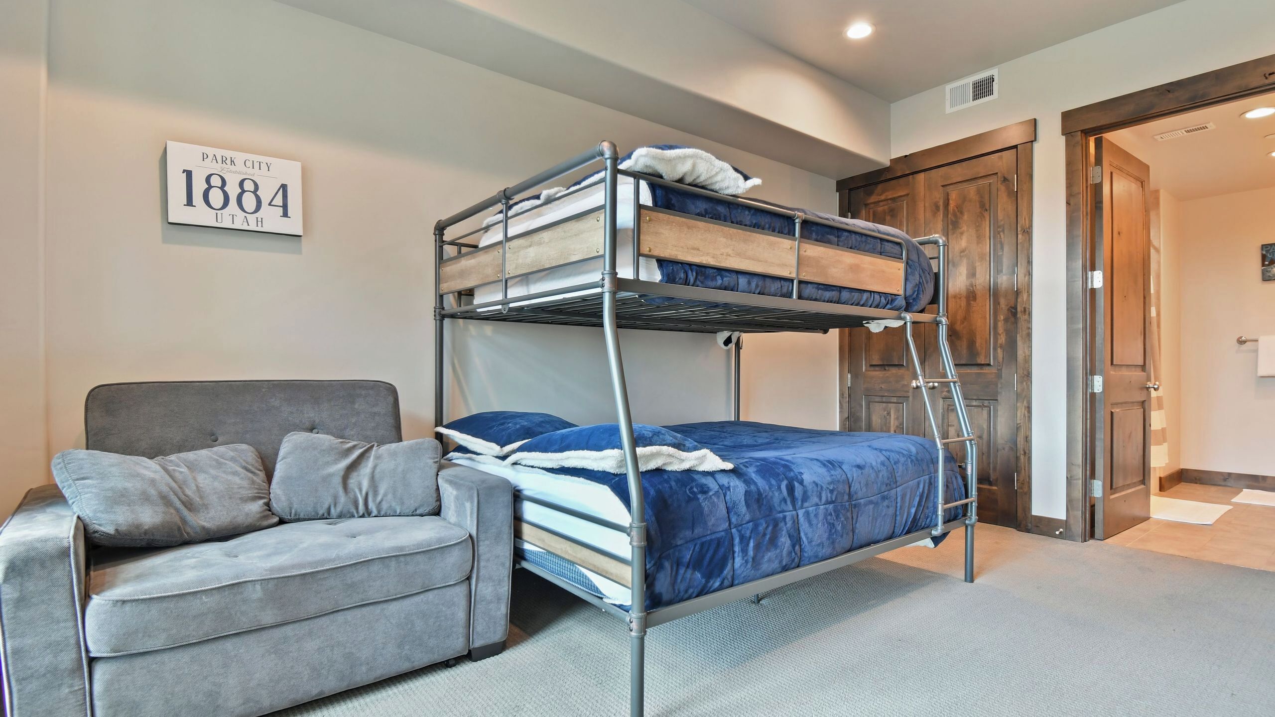 Een stapelbed met een ladder, een grijze bank met kussens en een bordje aan de muur.