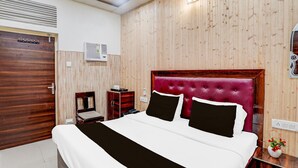A bedroom with a wooden panel wall, a bed with a red headboard, a bedside table, a chair, and an air conditioning unit. - Collection O Tajganj West Gate (Agra)