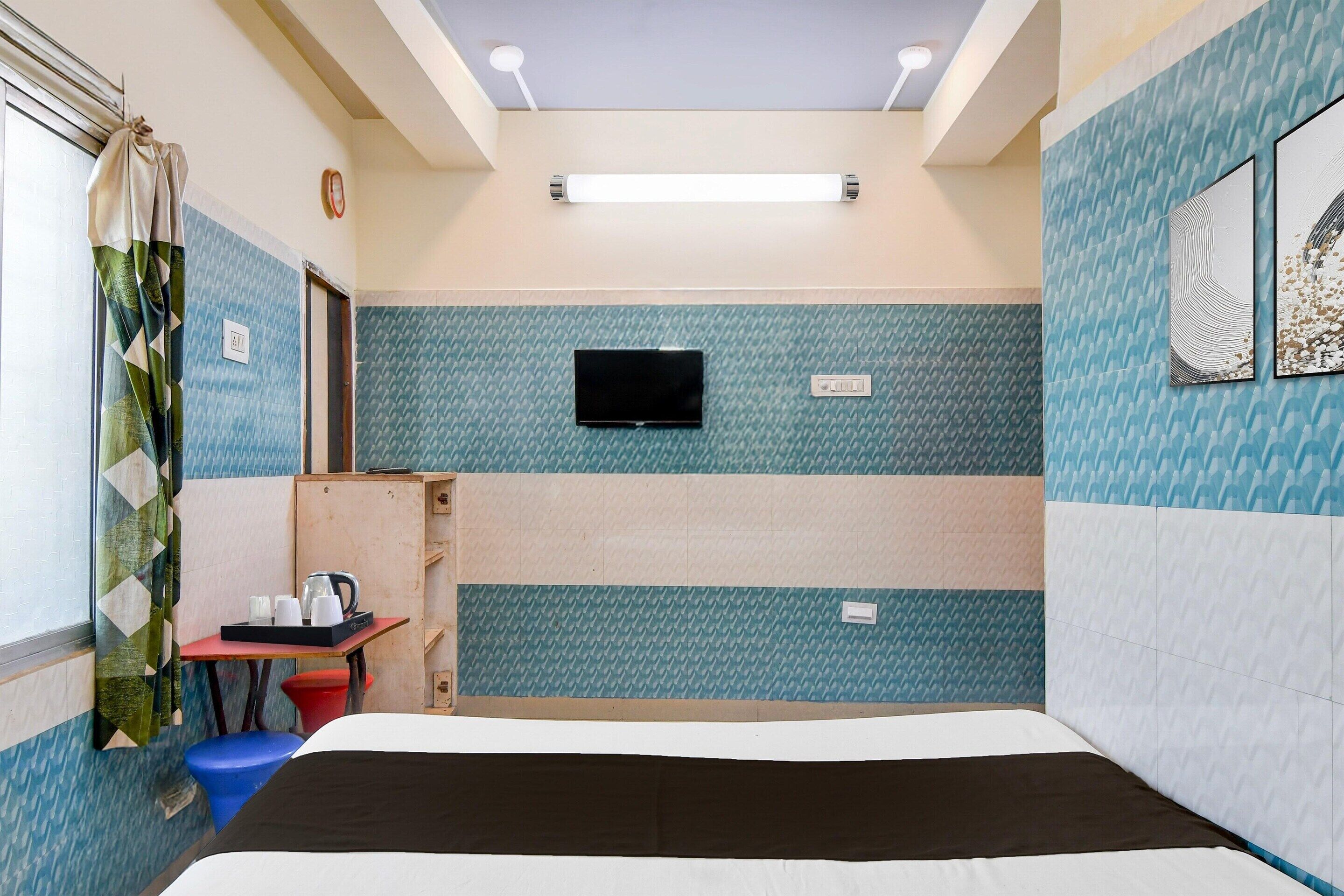 Habitación de hotel con cama, televisión, una mesita con tetera y ventana con cortinas.