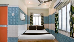 A bedroom with a bed, a ceiling fan, an air conditioning unit, a window with curtains, and a wall-mounted light switch. - Classic With Balcony Shibpur Tram Depot (Howrah)