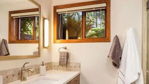 A bathroom with two sinks, wooden cabinets, a large mirror, and a window with a view of trees.