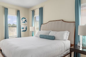 Une chambre d’hôtel avec un grand lit, deux tables de chevet, une petite table et une fenêtre avec des rideaux.