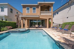 Ein zweistöckiges Haus mit Swimmingpool, Balkon und Terrasse mit Liegestühlen.