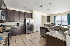 A modern kitchen with dark cabinets, stainless steel appliances, a granite countertop, and a tiled floor. - 6BR Reunion Escape w/ Pool, Spa & Outdoor Patio (Kissimmee)